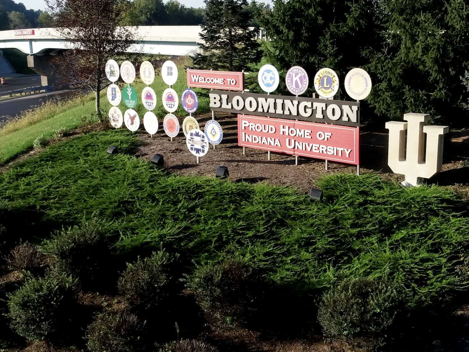 Colourful Bloomington welcome sign with various community and university logos, vibrant landscaping, and Indiana University emblem.
