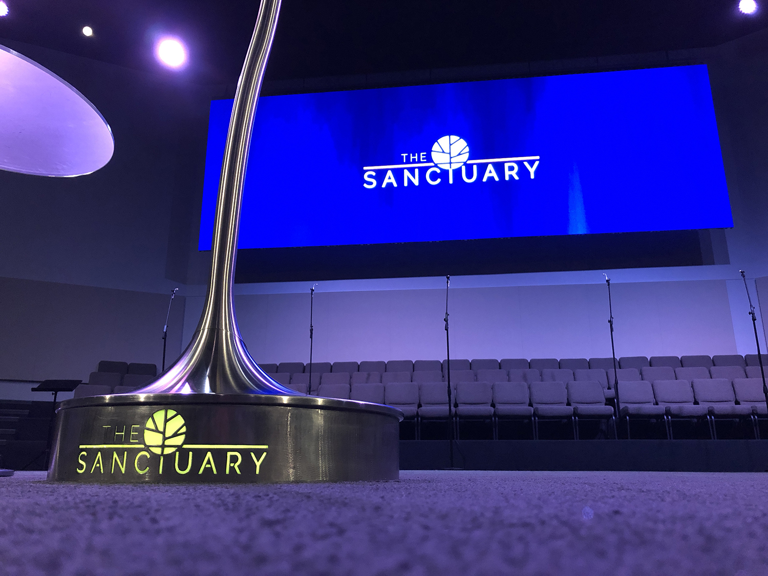 Modern conference stage with illuminated "The Sanctuary" logo and large digital screen.