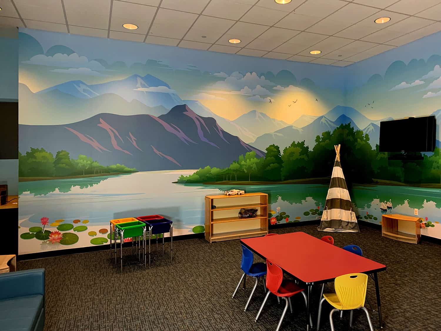 Vibrant nature-themed mural painted on classroom wall with mountains, river, and trees.