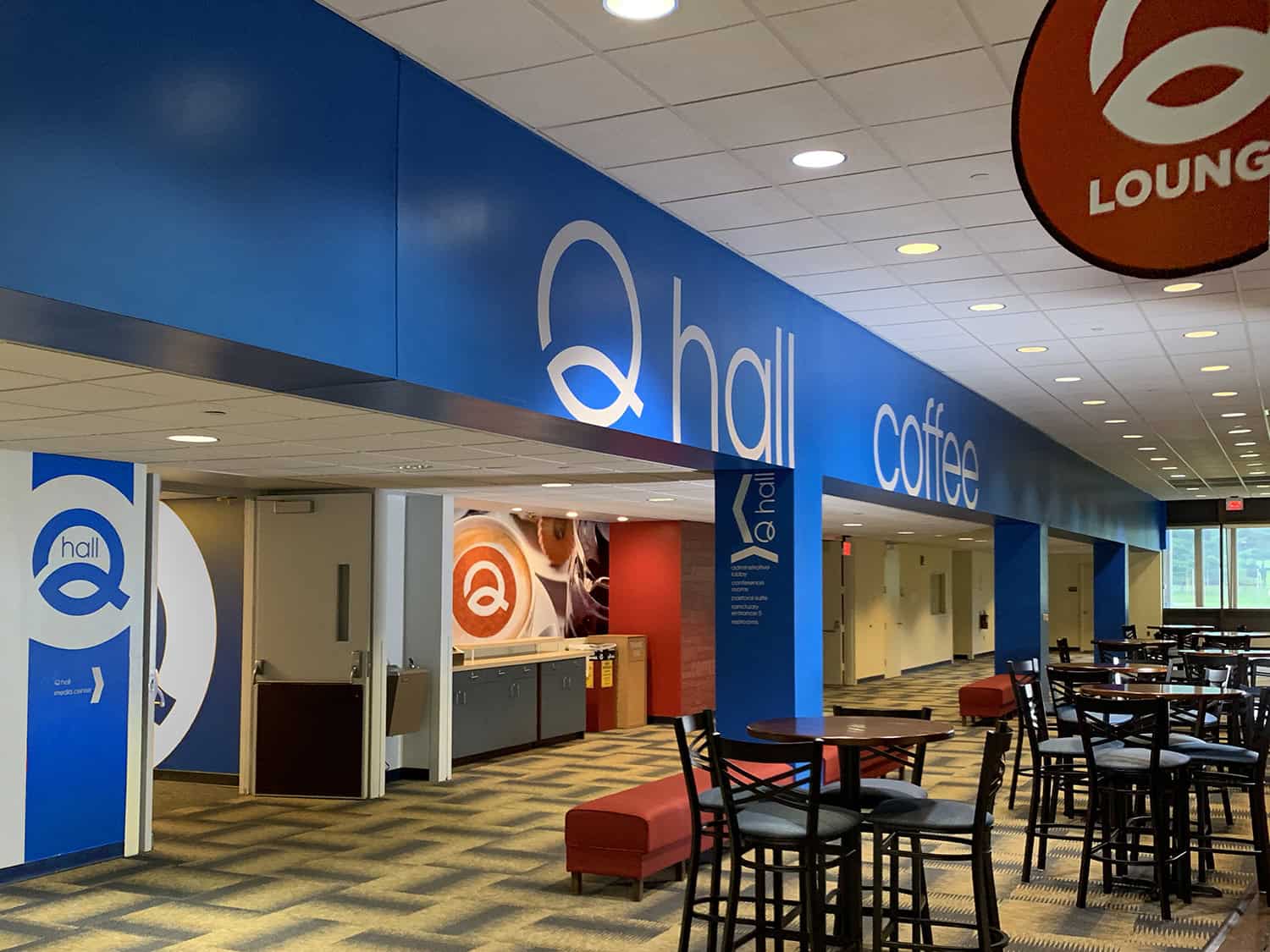 Large modern signage for Hall Q with vibrant blue background and white text, in a busy indoor lounge area.