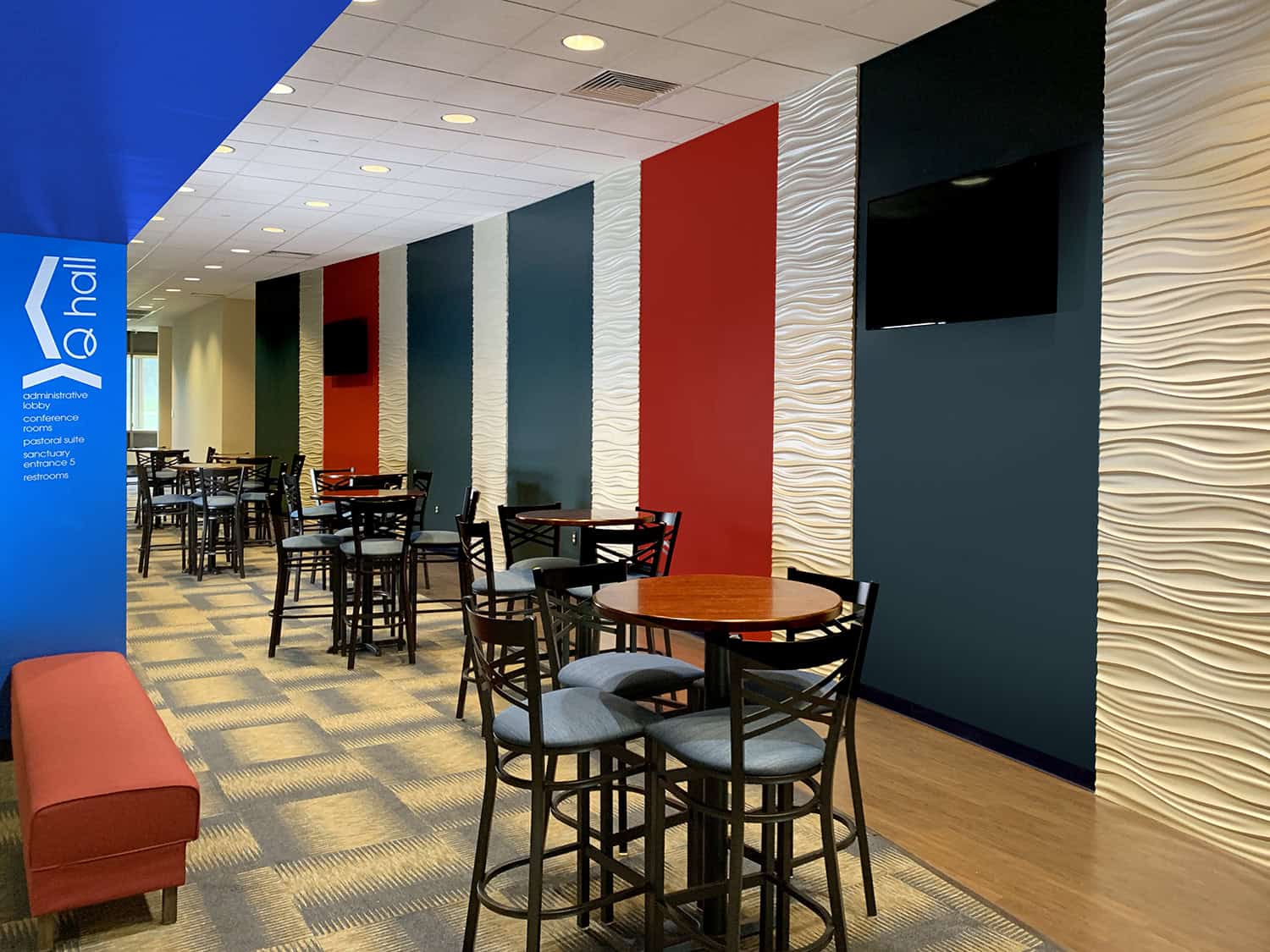 Bright modern church interior with textured wall panels and TV screens, welcoming space.