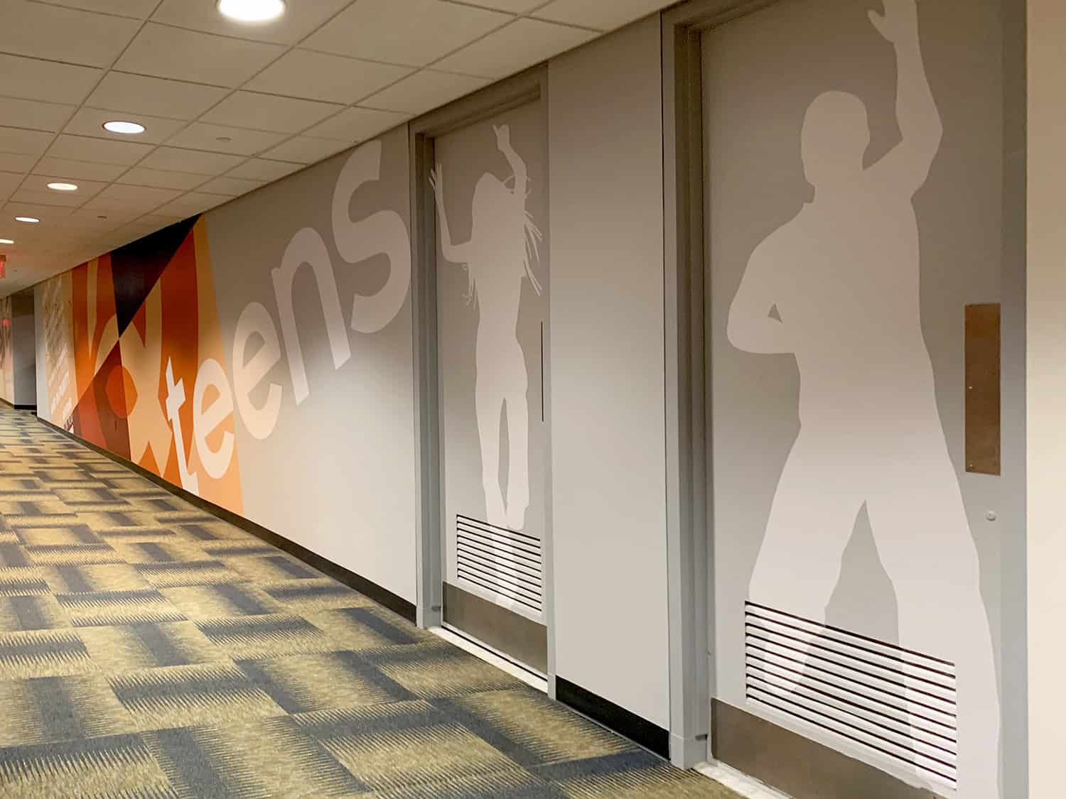 Modern office hallway wall graphic displaying fitness and wellness silhouettes and branding.