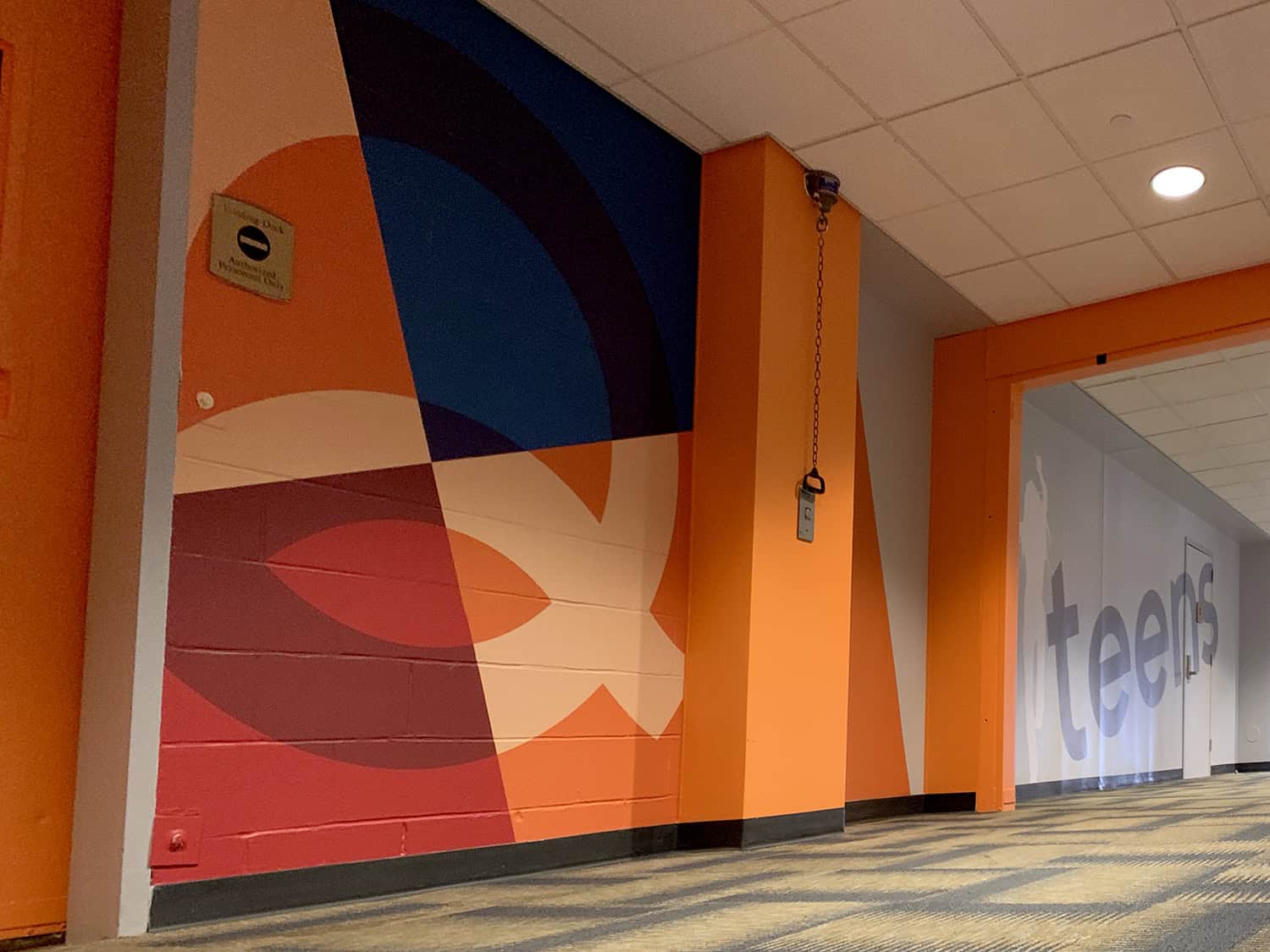 Vibrant geometric mural wall art with bold orange, blue, and red colours in office corridor.