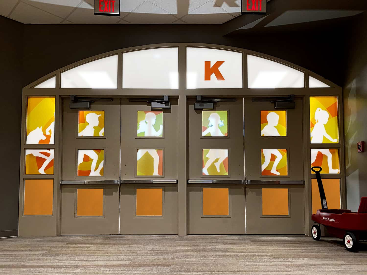 Colourful school entrance door with silhouette figures and signage for children’s activity area.