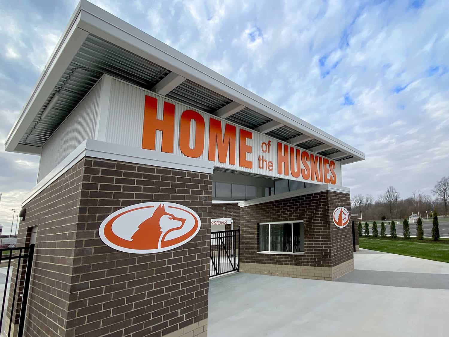 Bold orange "HOME of the HUSKIES" sign on modern building with husky logos, showcasing custom signage for schools or facilities.
