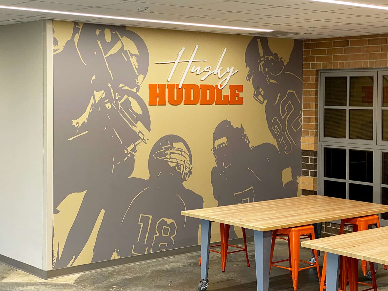 Vibrant wall mural featuring football players with signwork branding for sports-themed interior design.