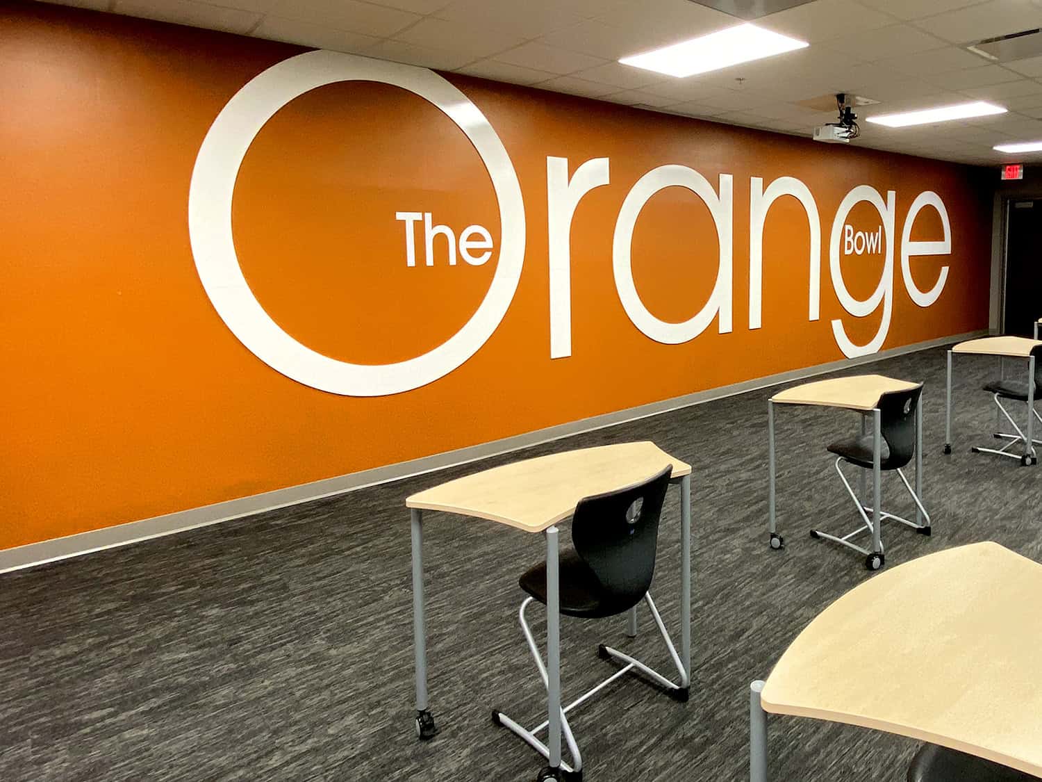 Bright orange wall with large white signage for The Orange Bowl, modern interior design.