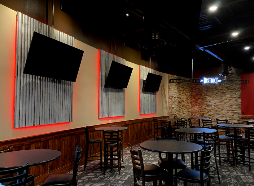 Brightly lit bar interior with multiple TVs, modern decor, and high tables.