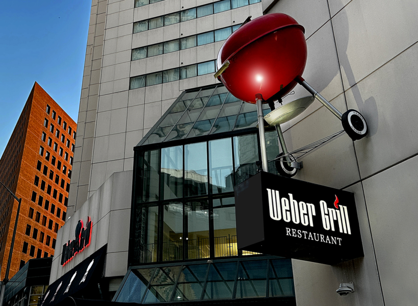 Bright red barbecue mascot sign for Weber Grill Restaurant on modern city building exterior.