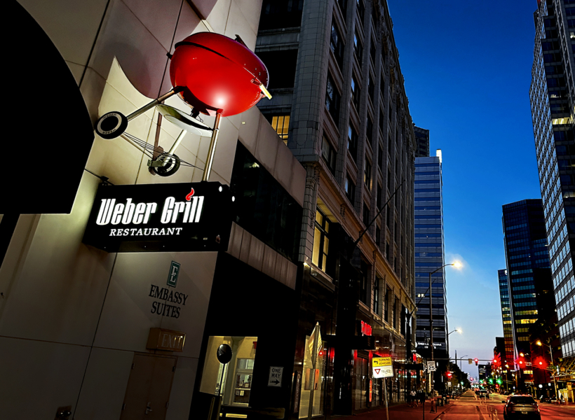 Vibrant city street with illuminated signs for Weber Grill Restaurant and Embassy Suites in downtown.