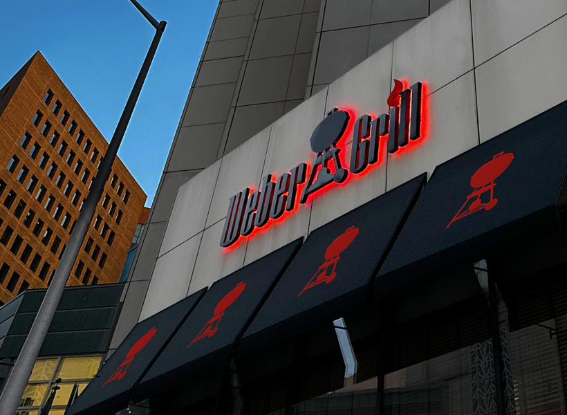 Vivid illuminated sign on building storefront with black awnings and red logo elements.