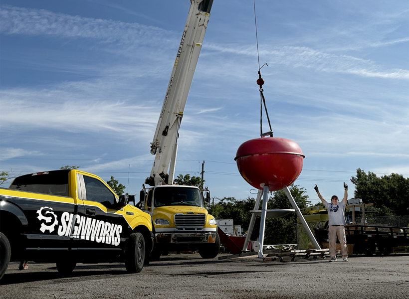 Crane lifting a large red sign for Signworks installation in daylight.