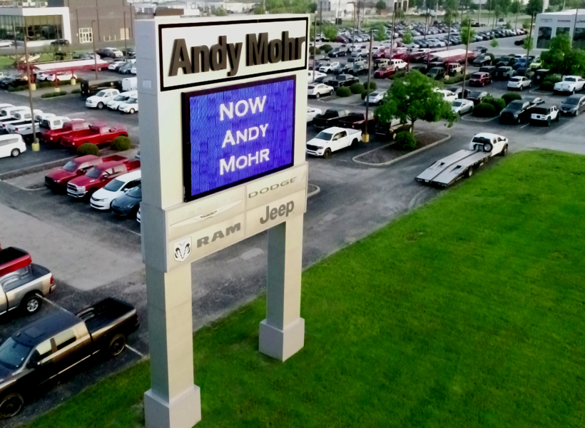Digital signboard displaying "NOW ANDY MOHR" advertising at car dealership.