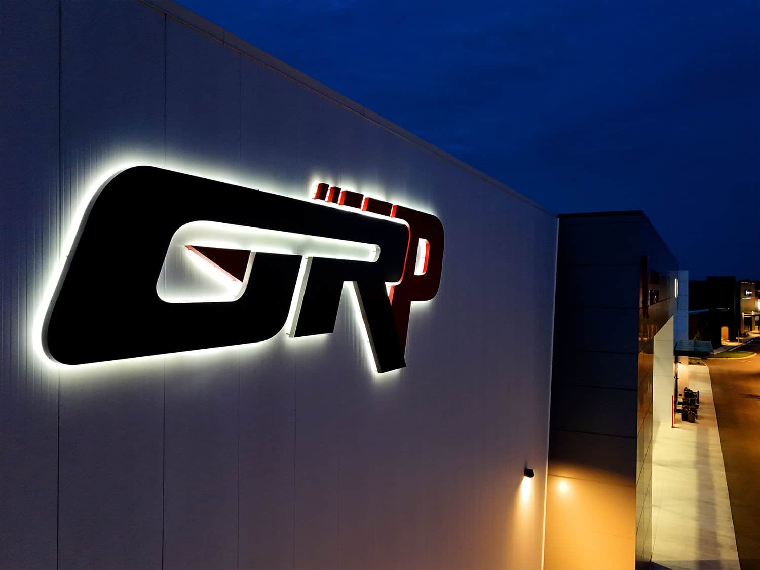 Backlit illuminated company logo sign on building exterior at night.