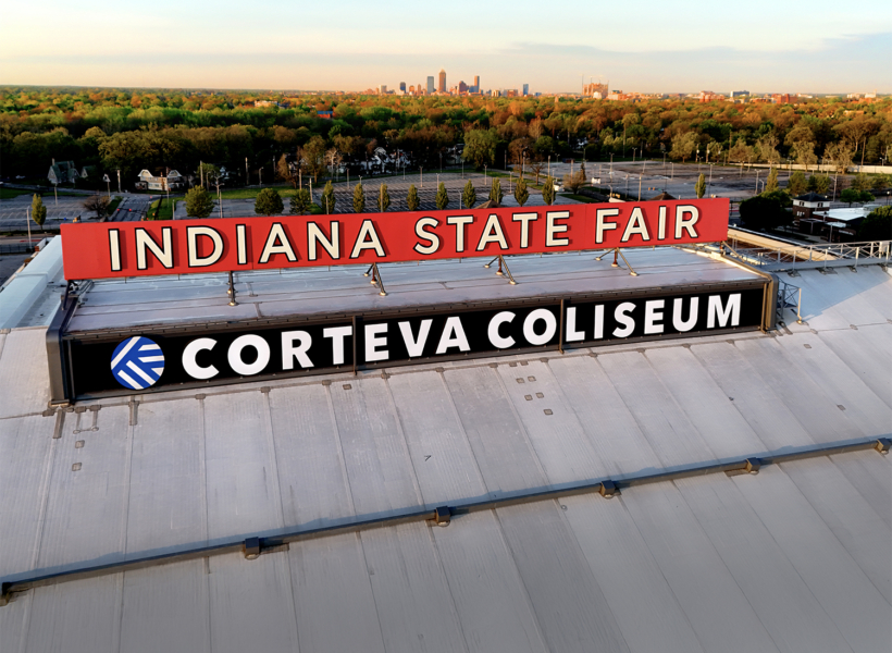 Bright Indianapolis State Fair sign on the Corteva Coliseum rooftop with city skyline in the background, leading signage solutions for events.