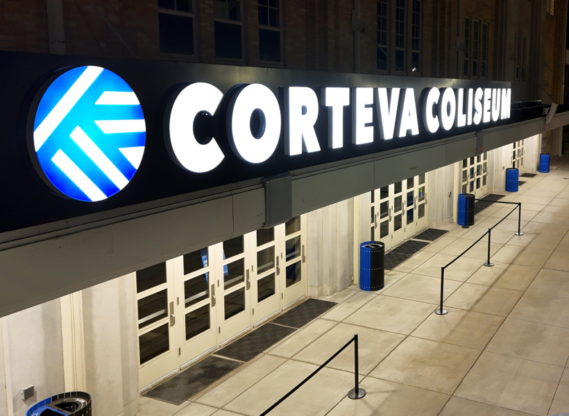 Illuminated sign for Corteva Coliseum with bold white lettering and logo at night.