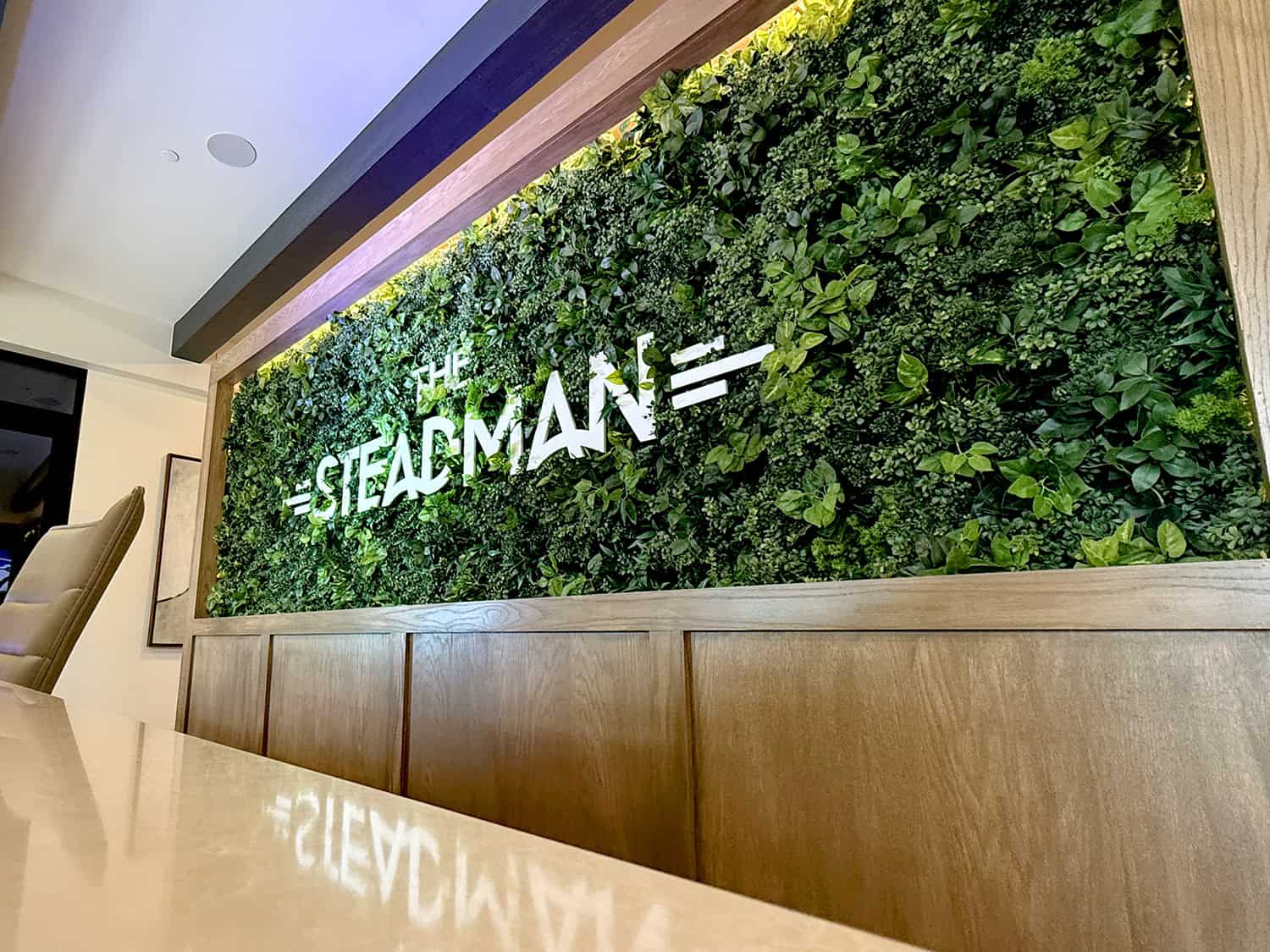 Lush green plant wall with illuminated "The Steadman" sign in modern office decor.